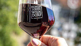 Ein mit Rotwein gefülltes Stielglas mit dem Logo des Hohenloher Weindorfs.
