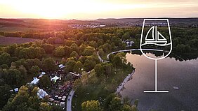 Blick auf den Breitenauer See im Sonnenuntergang, davor in weiß das Wein-am-See-Logo (ein stilisierten Weinglas, in dem ein Segelboot schwimmt)