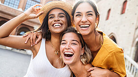 Drei lachende junge Frauen in Sommeroutfits auf Städtetrip in Frankreich.