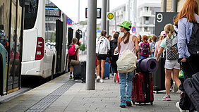 Eine Mädchengruppe und ihre Betreuerinnen laufen mit Reisegebäck zum Bus.
