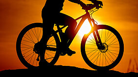 Silhouette eines Radfahrers auf dem Gipfel eines Bergs im Sonnenuntergang